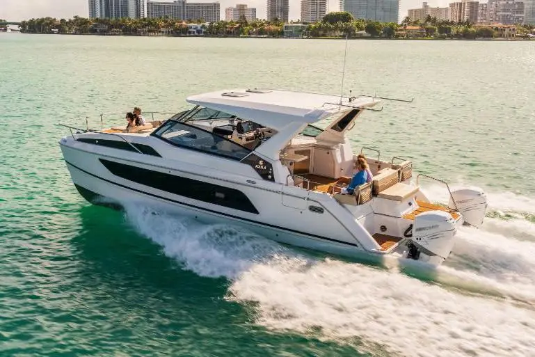 Luxury motorboat cruising through turquoise waters, with two people onboard and city skyline in the background.
